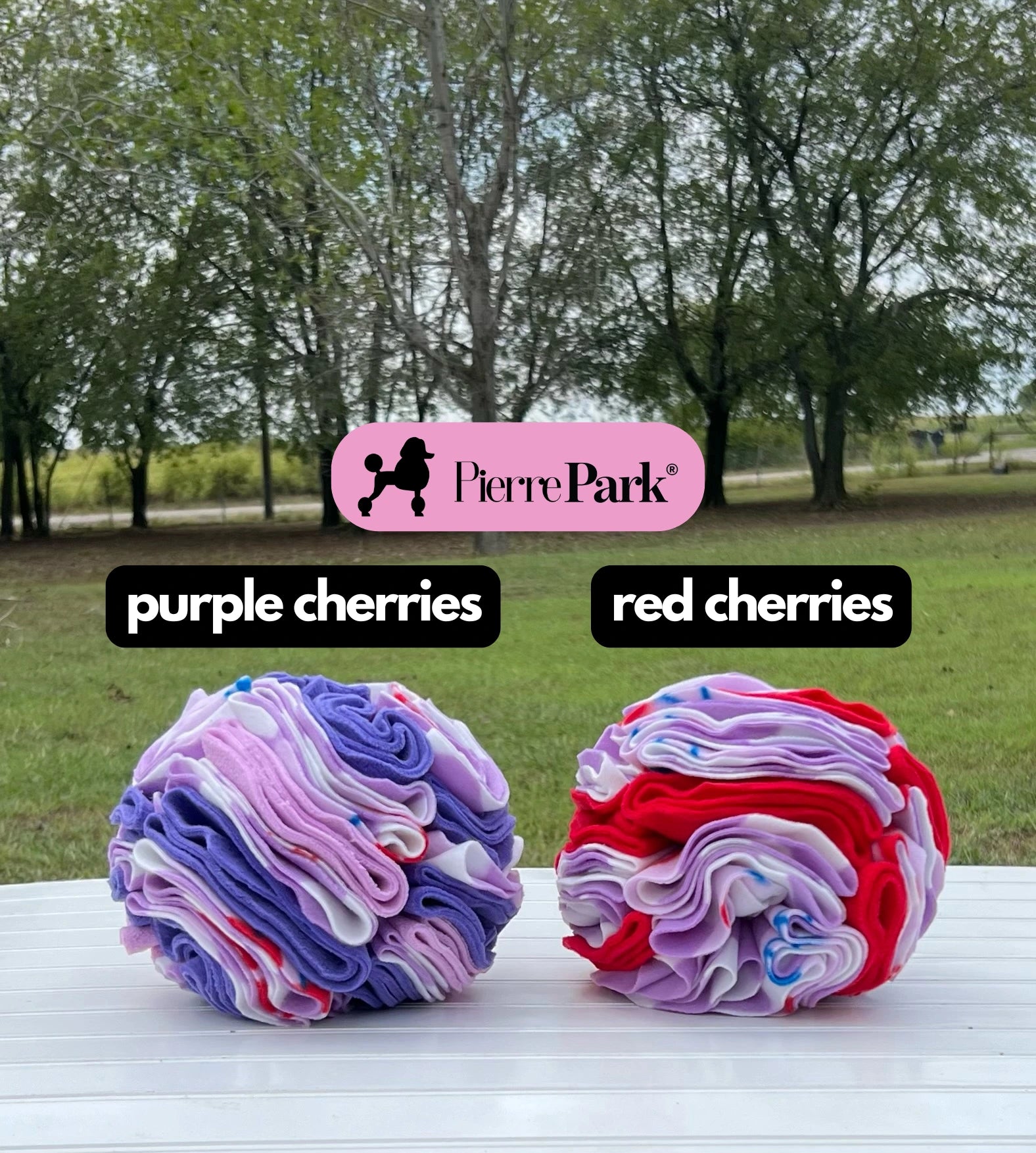 Snuffle ball for dogs by PierrePark, 'purple cherries' and 'red cherries', presented outdoors on a table against a scenic tree background. These richly colored toys stimulate dogs' natural foraging behaviors and provide sensory enrichment.