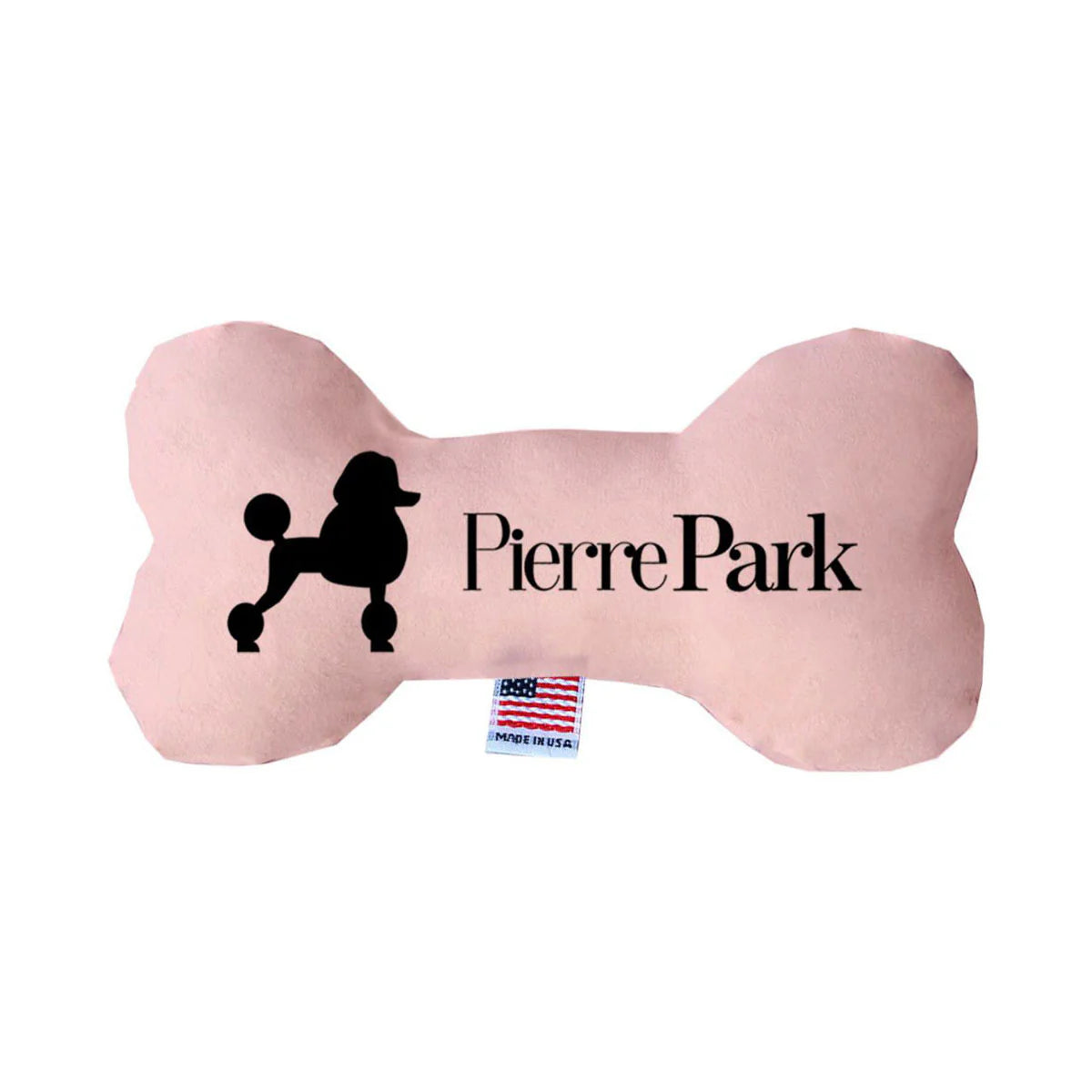 The Pink Dog Bone Toy by PierrePark is light pink, bone-shaped, featuring a black Pierre Park label, a poodle silhouette, and a small tag with an American flag design.