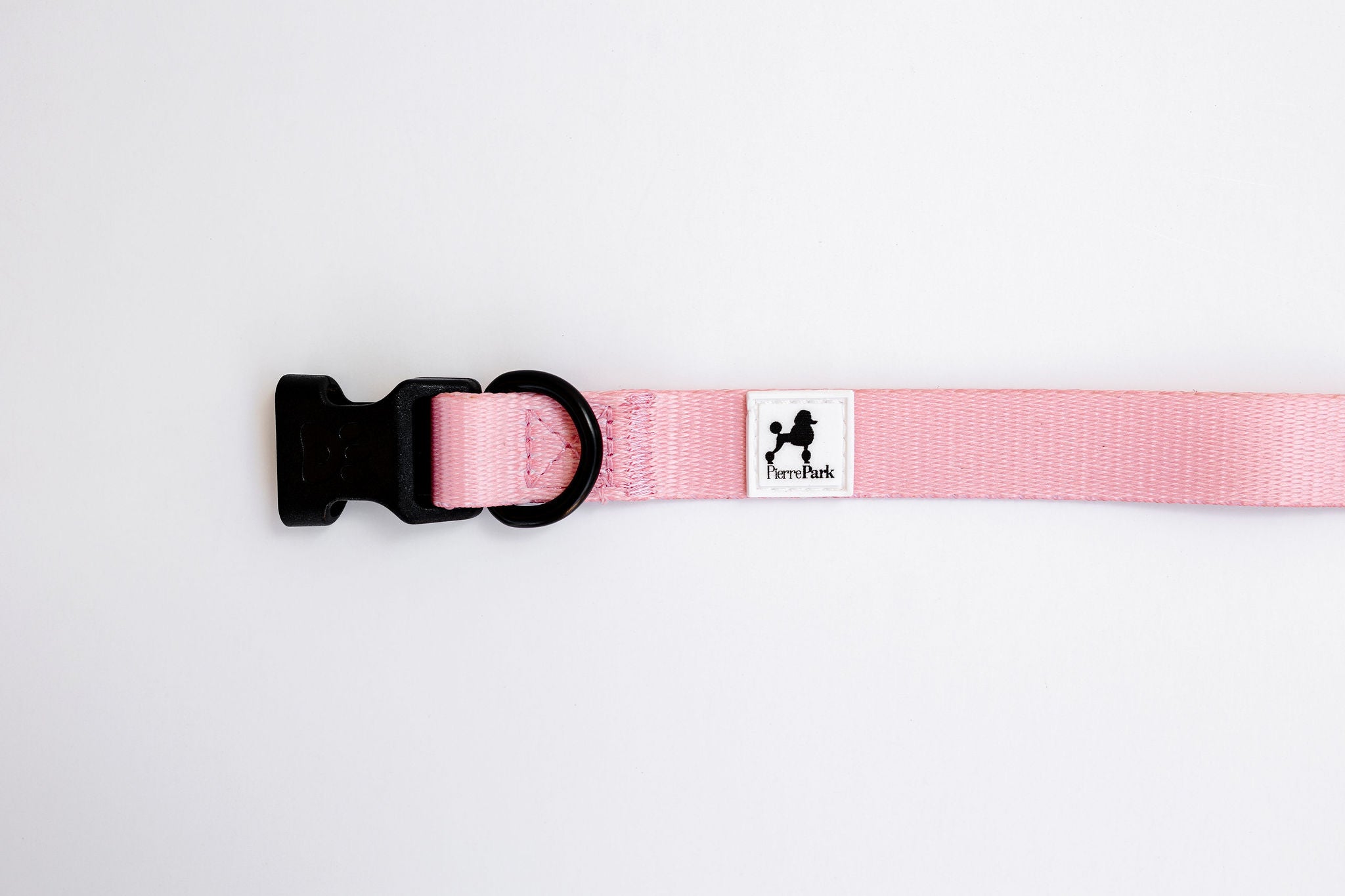 The Pink Dog Collar by PierrePark features a black plastic buckle and ring, along with a small patch depicting a cartoon dog silhouette and the text PawPark, shown against a plain white background.