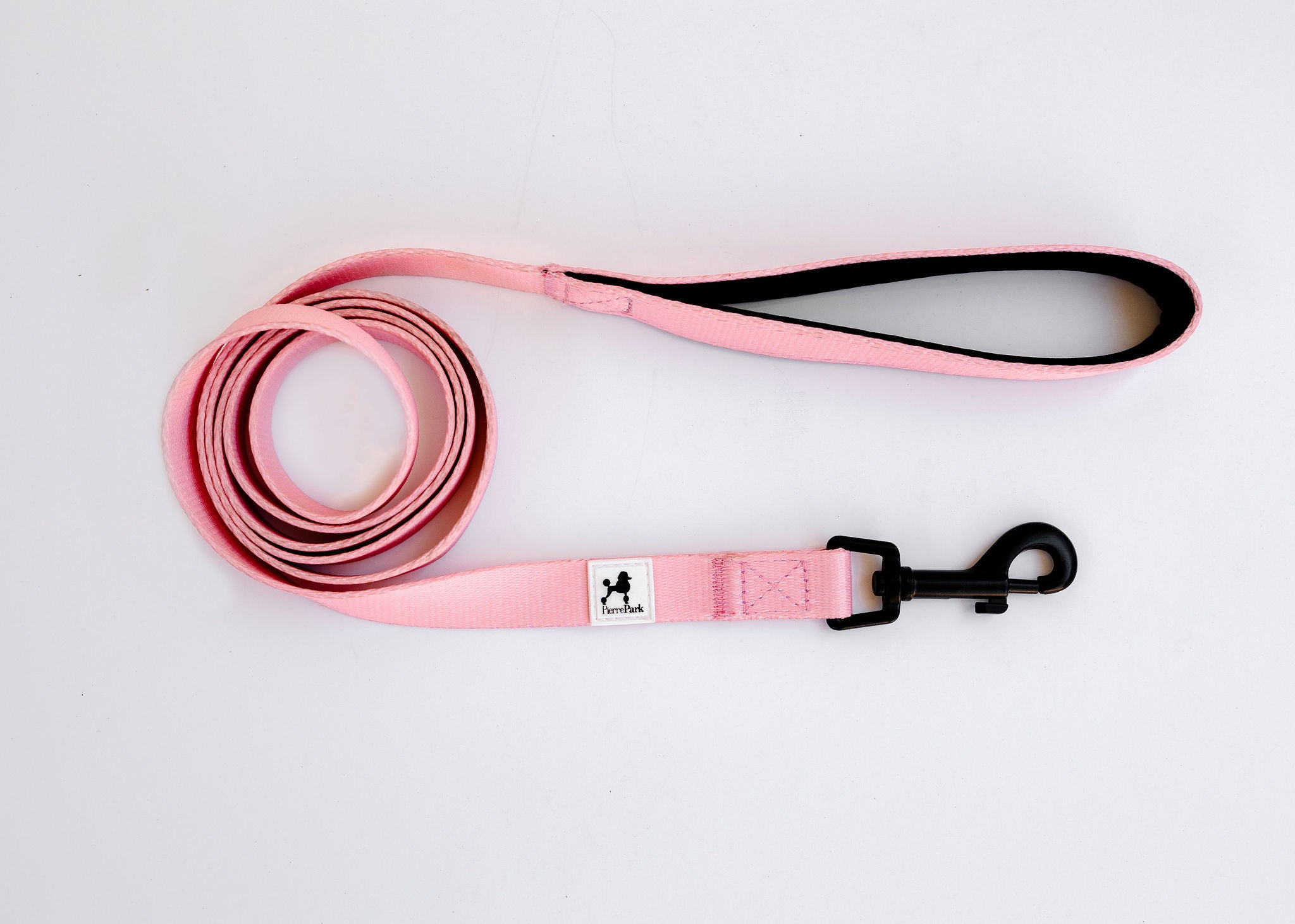 The Pink Dog Leash by PierrePark, featuring a black handle and metal clip, is neatly coiled on a white background.