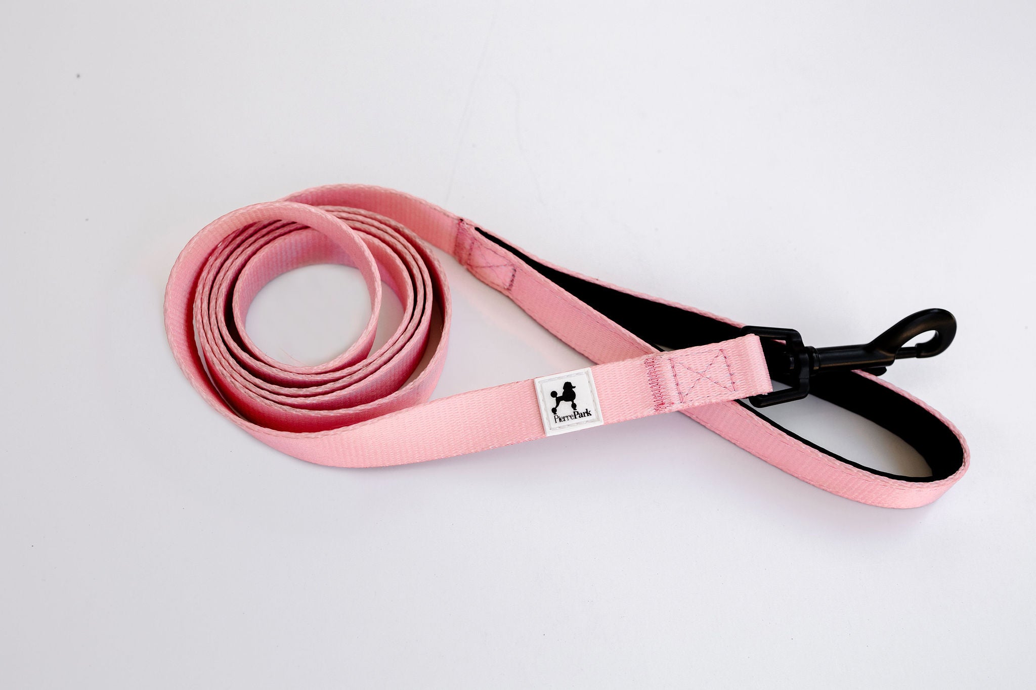 The Pink Dog Leash by PierrePark is coiled, pink, features a black clasp, and has a small label with a dog silhouette on a white background.