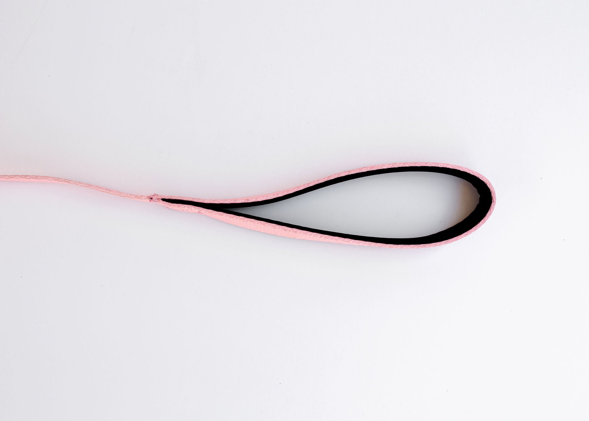 The Pink Dog Leash by PierrePark lies on a white surface in an oval loop with the pink exterior section and black interior. The leashs free end extends to the left.