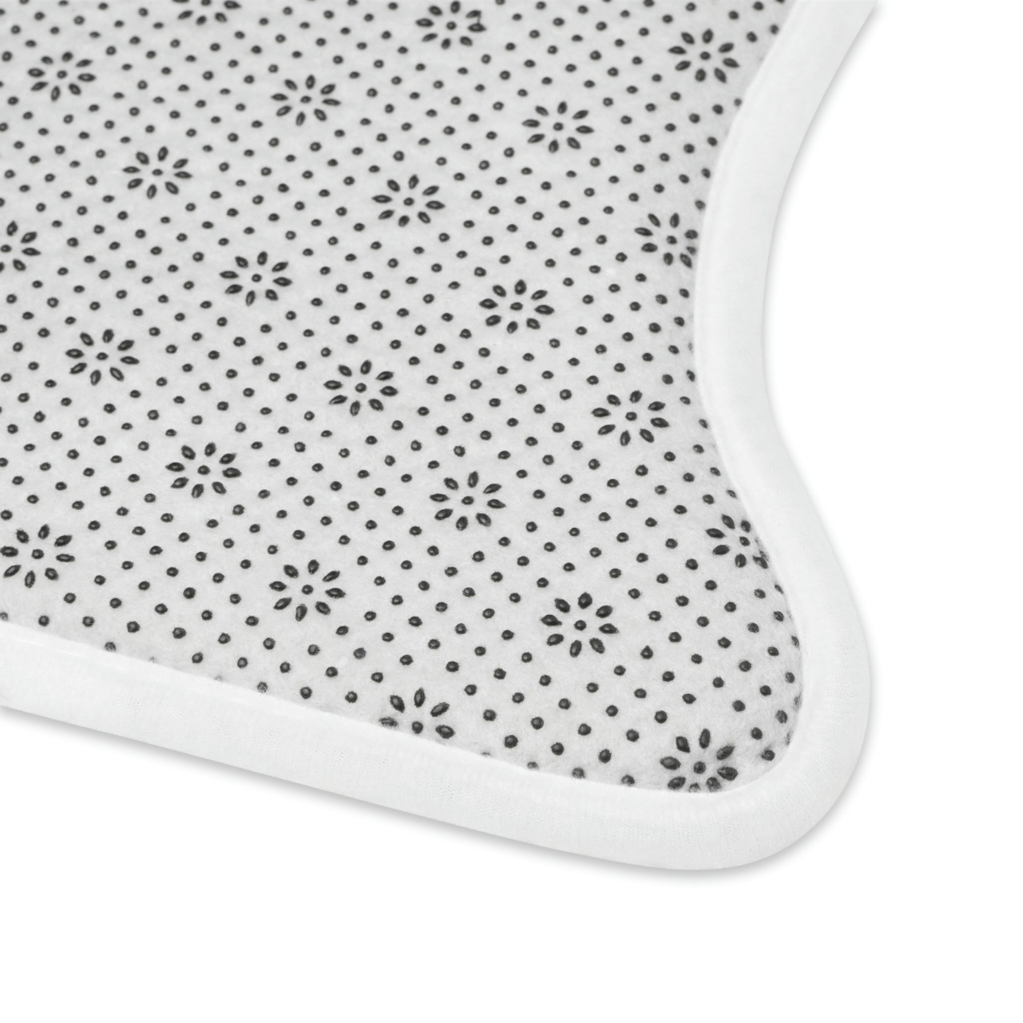 Close-up of a pink fabric featuring a pattern of small black flowers and dots, designed with a curved edge and white border. The PierrePark Dog Food Mat - Pink features a non-slip bottom for added stability during use.
