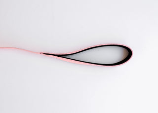 The Pink Dog Leash by PierrePark lies on a white surface in an oval loop with the pink exterior section and black interior. The leashs free end extends to the left.