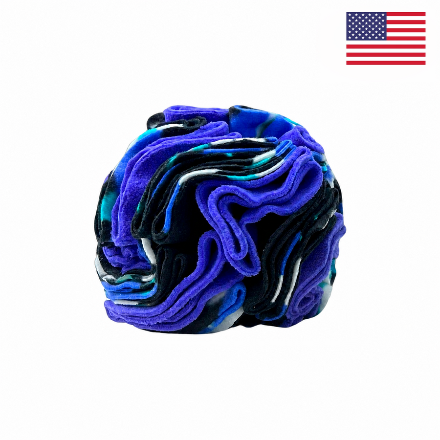 The PierrePark Snuffle Ball for Dogs – Purple Fireflies is a rolled, multicolored fabric featuring blue, purple, black, and white swirls on a white background—designed as an interactive puzzle toy. A small U.S. flag appears in the top right corner, highlighting that this product is proudly made in the USA.