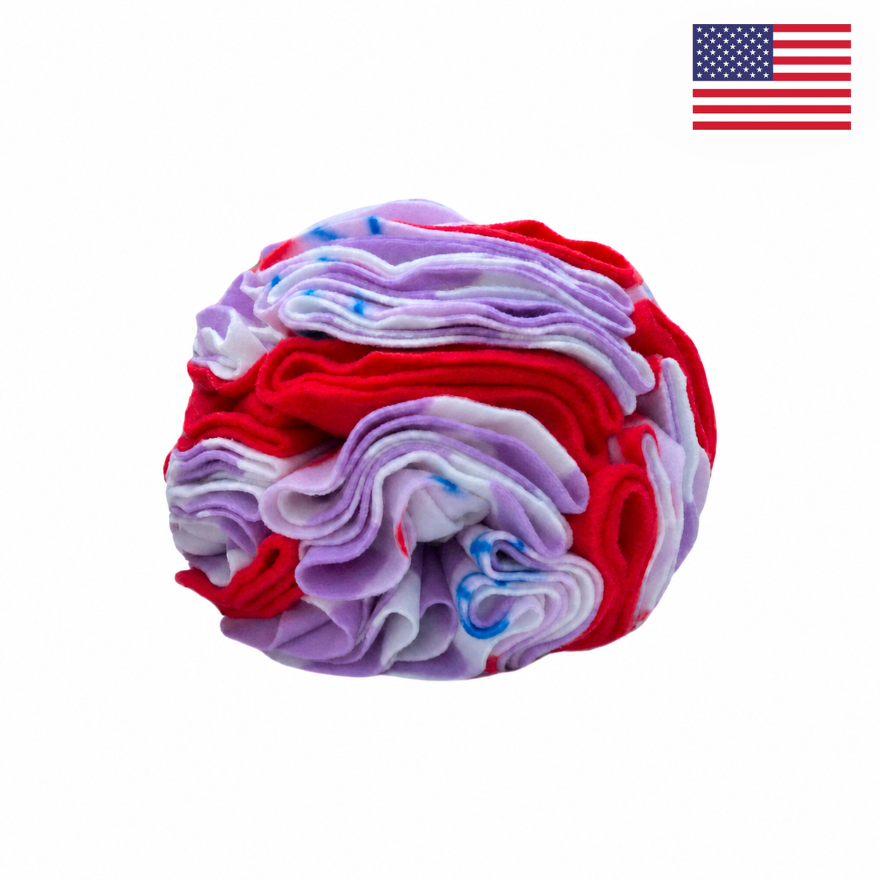 A ball-shaped bundle of tie-dyed fabric in vibrant red, white, and blue hues is featured, resembling the Snuffle Ball for Dogs – Red Cherries by PierrePark. A small American flag appears in the top right corner, emphasizing that this interactive puzzle toy is made in the USA. The background is plain white.